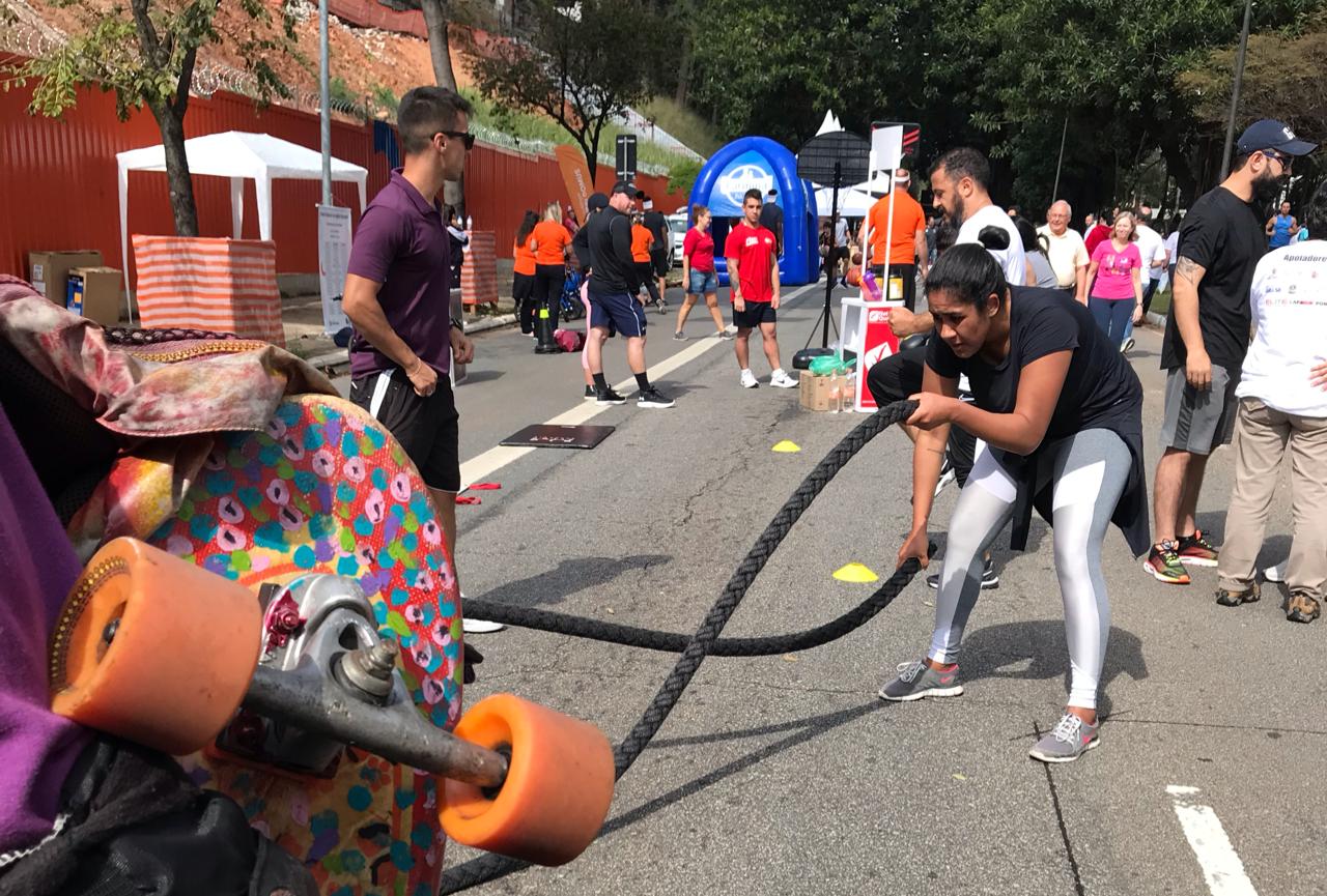 Atividade em uma corda é praticada por uma mulher. Na foto aparece ainda parte de um skate e outras pessoas ao fundo com vestes esportivas 